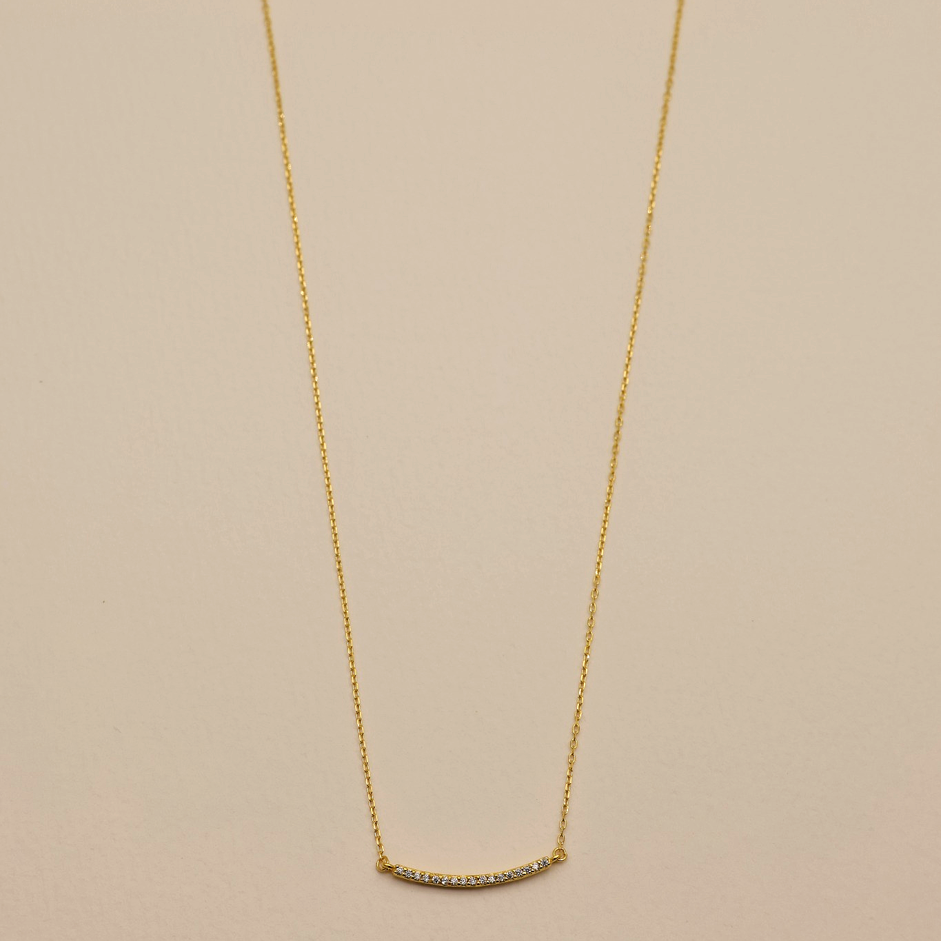 Flat lay of Clémence Bar Necklace in gold vermeil with cubic zirconia on cream background