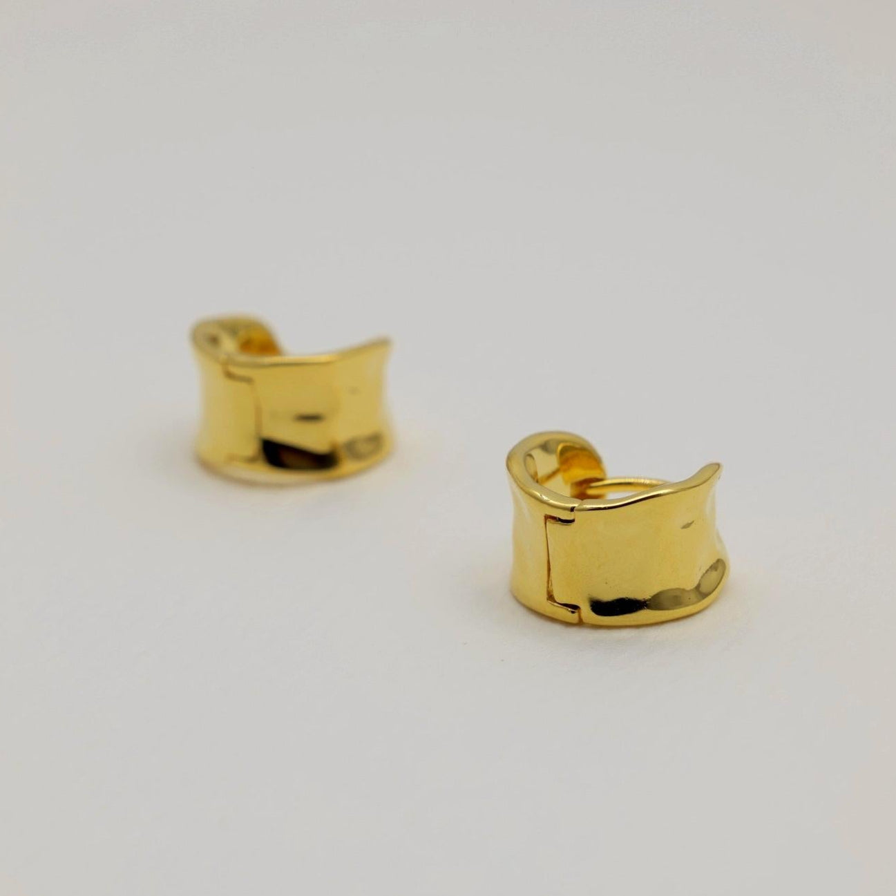 A pair of small gold vermeil mini hoop earrings with a polished, curved surface and hinge clasp, shown on a neutral background.
