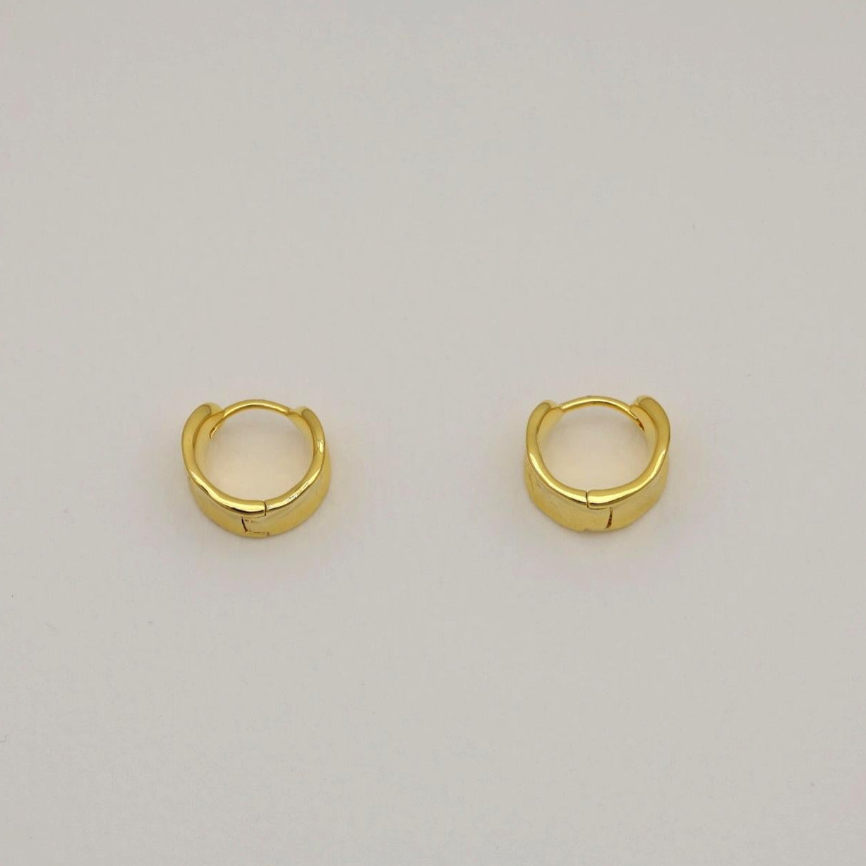 A pair of small gold vermeil mini hoop earrings with a polished, curved surface and hinge clasp, shown on a neutral background.