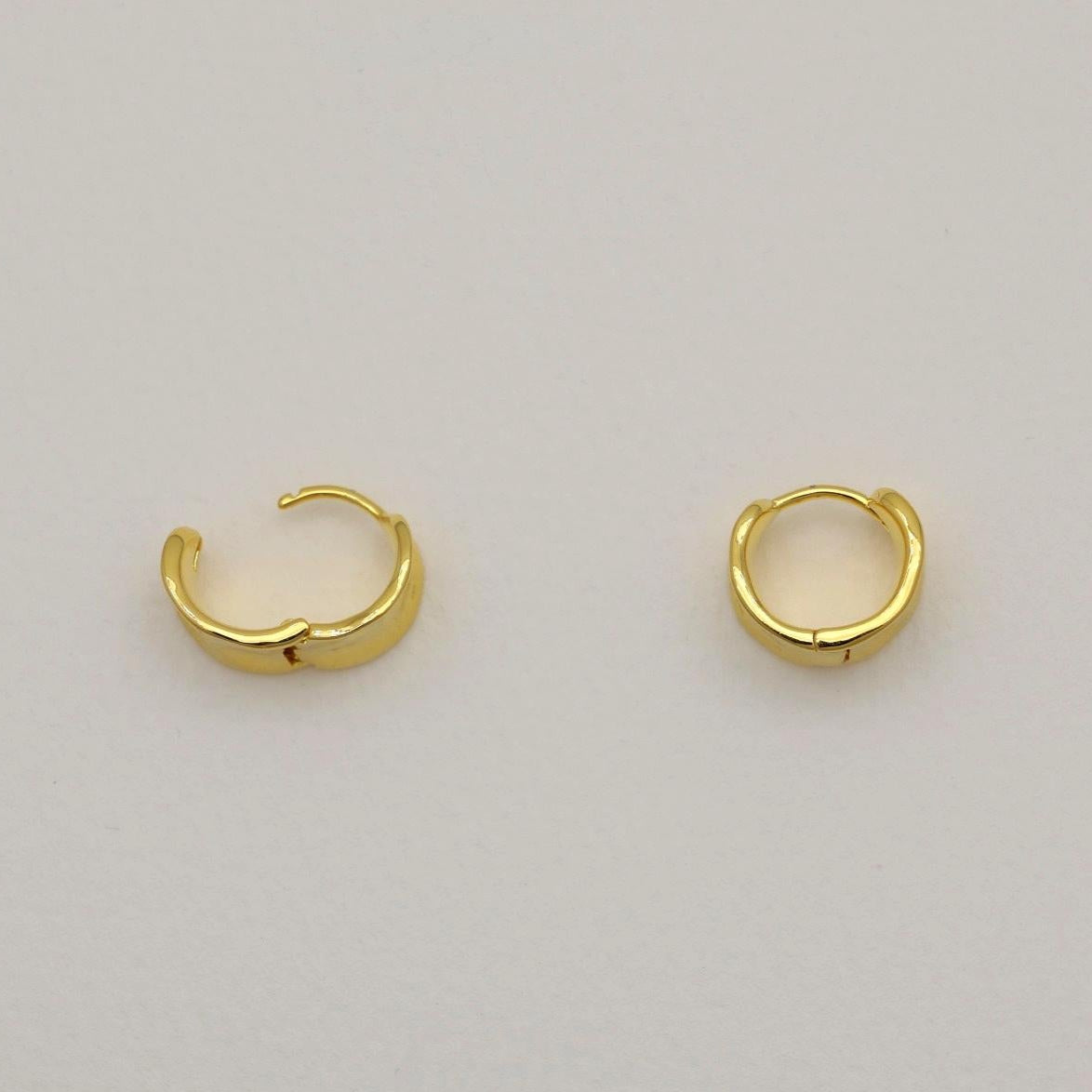 A pair of small gold vermeil mini hoop earrings with a polished, curved surface and hinge clasp, shown on a neutral background.