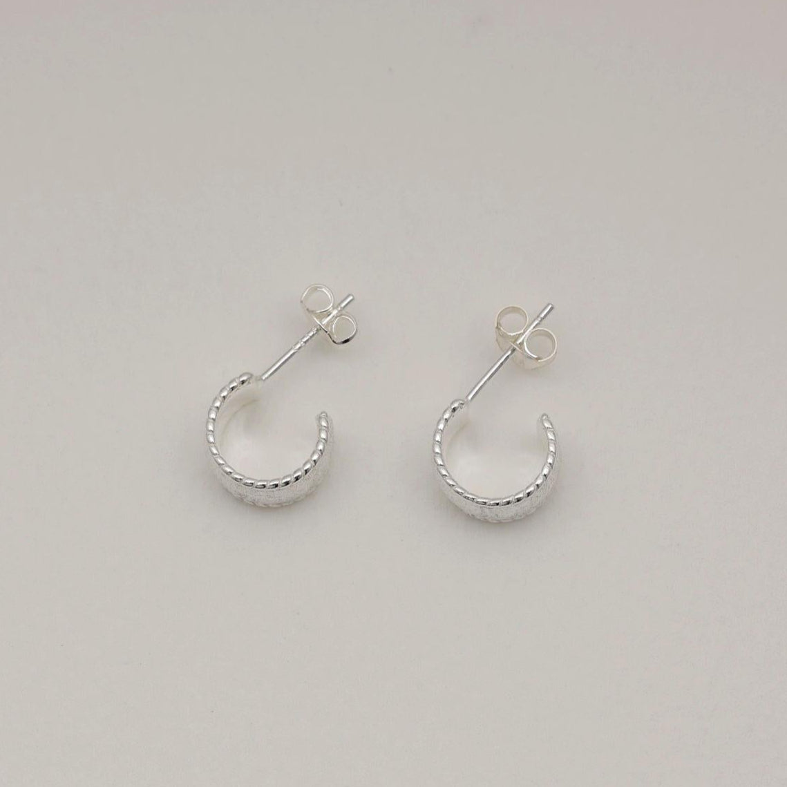 Sterling silver huggie earrings with a wide textured band and polished beaded edge, softly sculpted with matte and glossy contrast.
