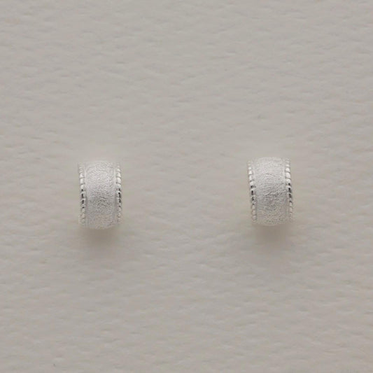 Sterling silver huggie earrings with a wide textured band and polished beaded edge, softly sculpted with matte and glossy contrast.