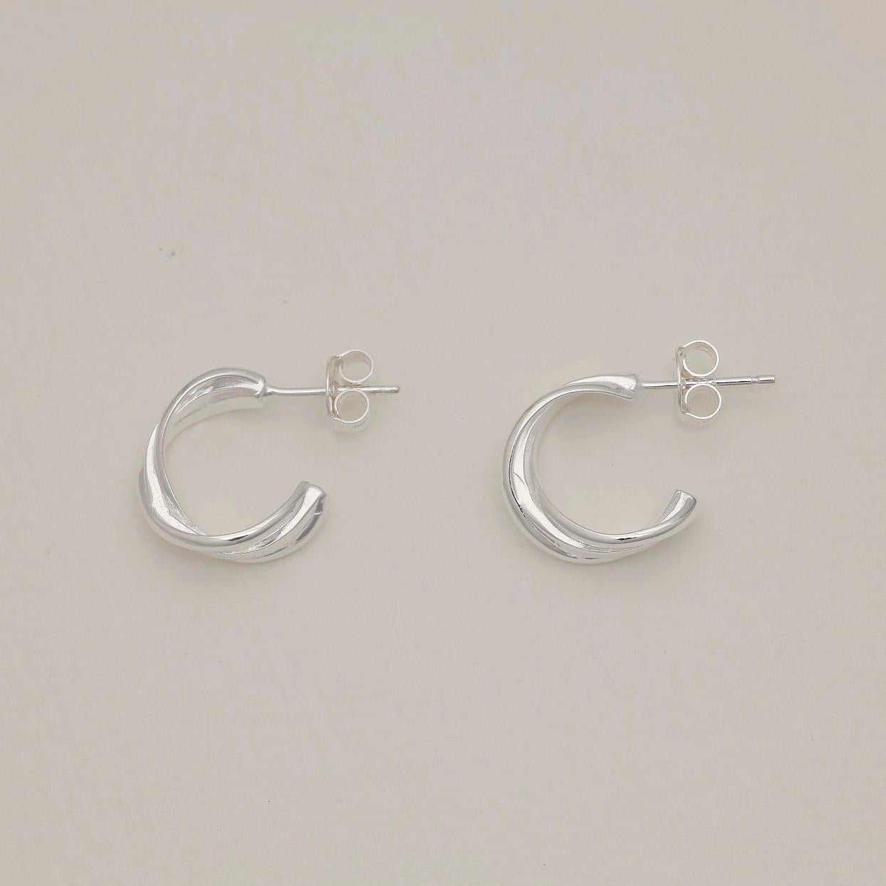 Pair of folded design sterling silver stud earrings on light background, soft polished finish