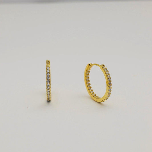 Close-up of gold vermeil pavé huggie earrings with cubic zirconia stones on neutral background