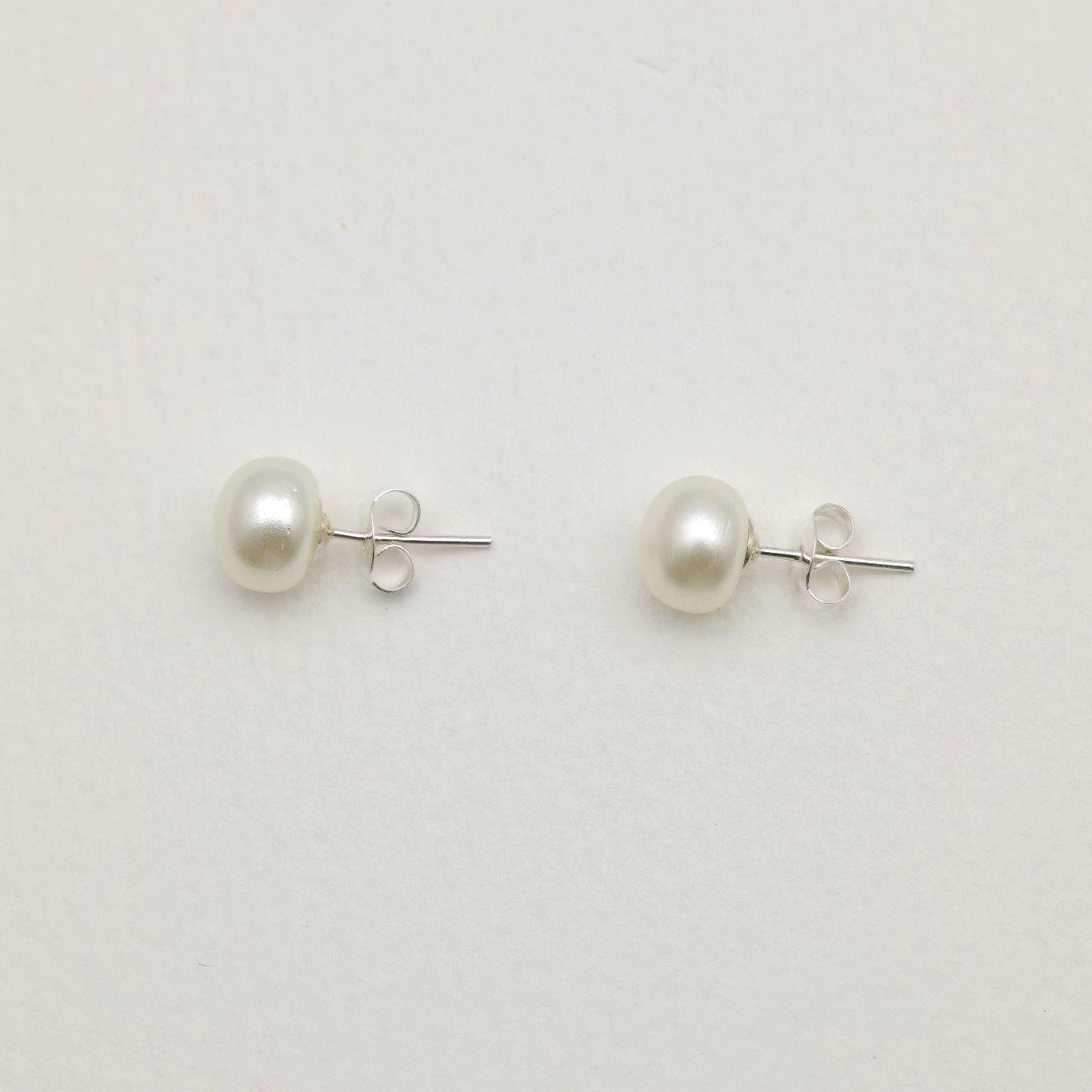 Close-up of 925 sterling silver pearl stud earrings on textured neutral background, showing round natural pearls with minimalist push-back posts.
