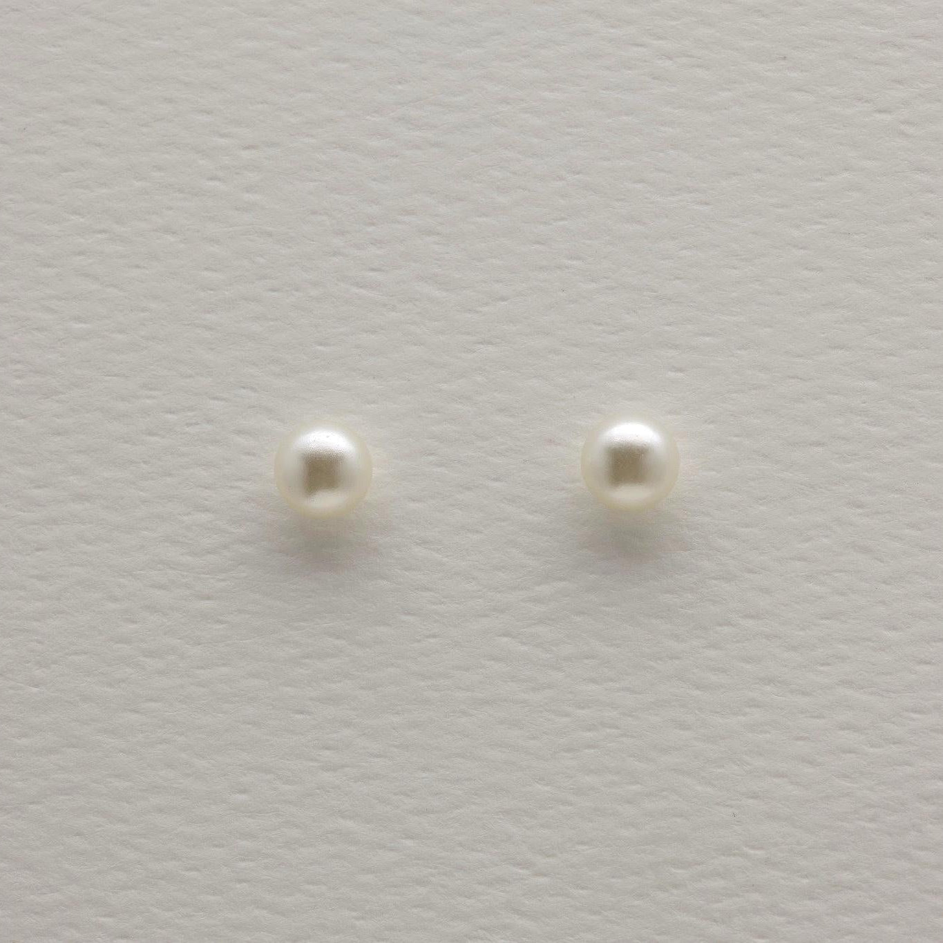Close-up of 925 sterling silver pearl stud earrings on textured neutral background, showing round natural pearls with minimalist push-back posts.