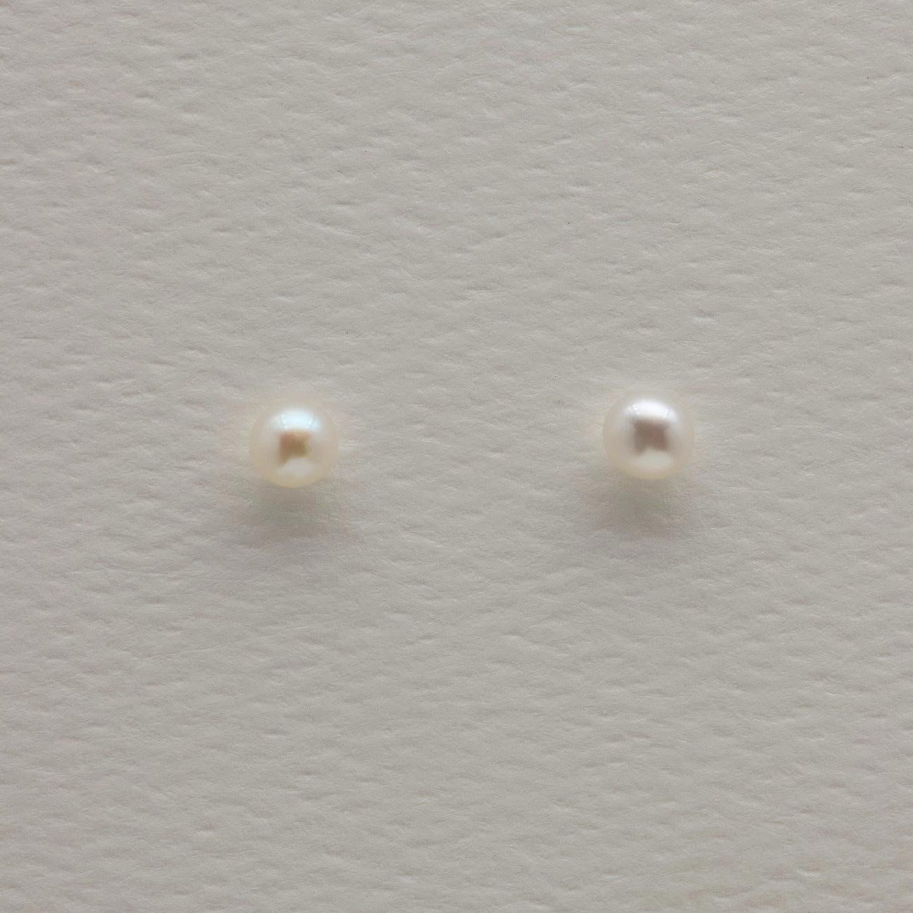 Close-up of 925 sterling silver pearl stud earrings on textured neutral background, showing round natural pearls with minimalist push-back posts.