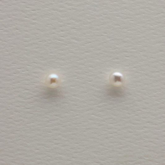 Close-up of 925 sterling silver pearl stud earrings on textured neutral background, showing round natural pearls with minimalist push-back posts.