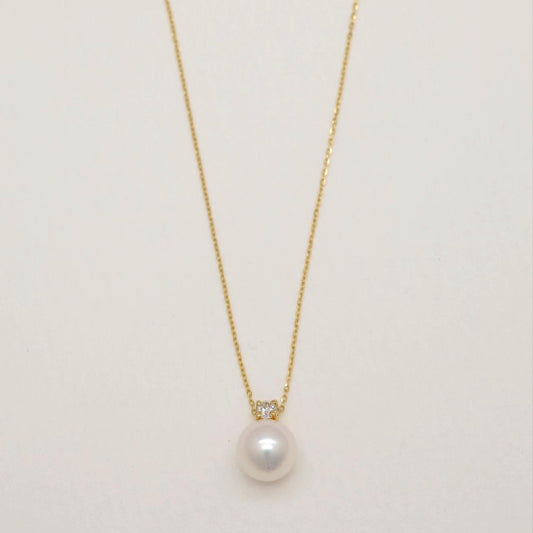 Close-up of 18K gold necklace with Akoya pearl and natural diamond pendant on a light background.
