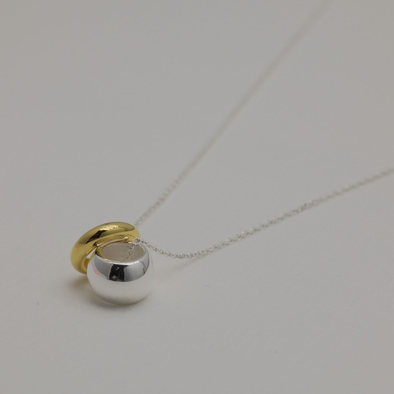 Close-up of the Léontine Necklace showing two polished donut pendants — one in gold vermeil, one in sterling silver — on a fine silver chain.