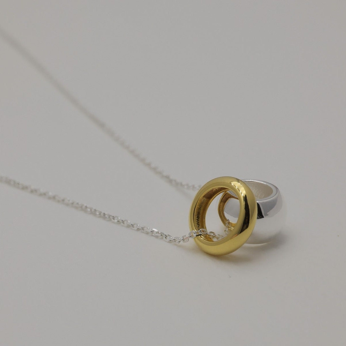 Close-up of the Léontine Necklace showing two polished donut pendants — one in gold vermeil, one in sterling silver — on a fine silver chain.