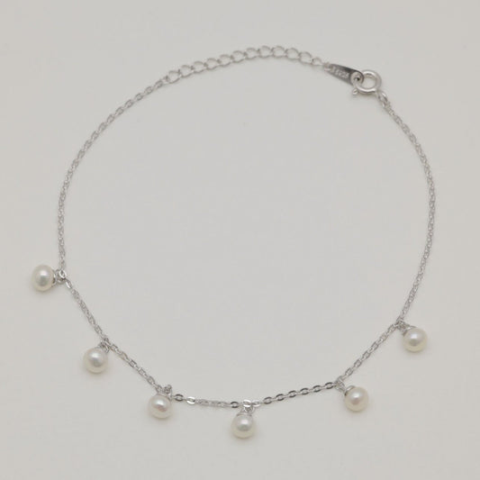 Sterling silver chain bracelet with six small natural pearl drops, photographed flat on a neutral background.