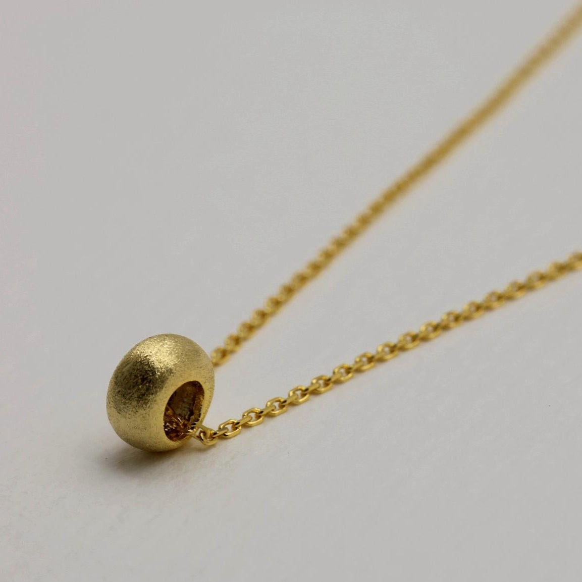 Close-up of softly frosted gold bead pendant on the Noémie necklace

