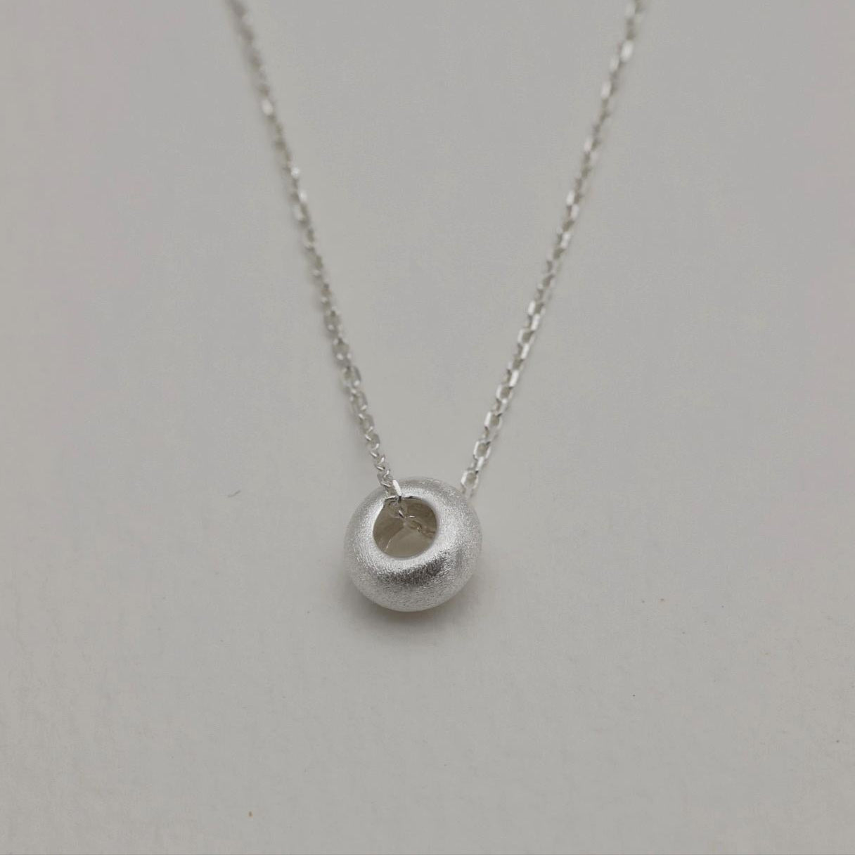 Close-up of the Noémie Necklace featuring a frosted silver bead on a delicate 925 sterling silver chain.