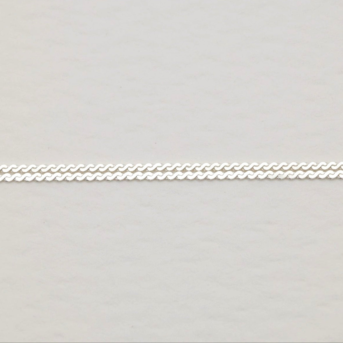 Close-up of interlinked dual chain pattern in sterling silver on cream background