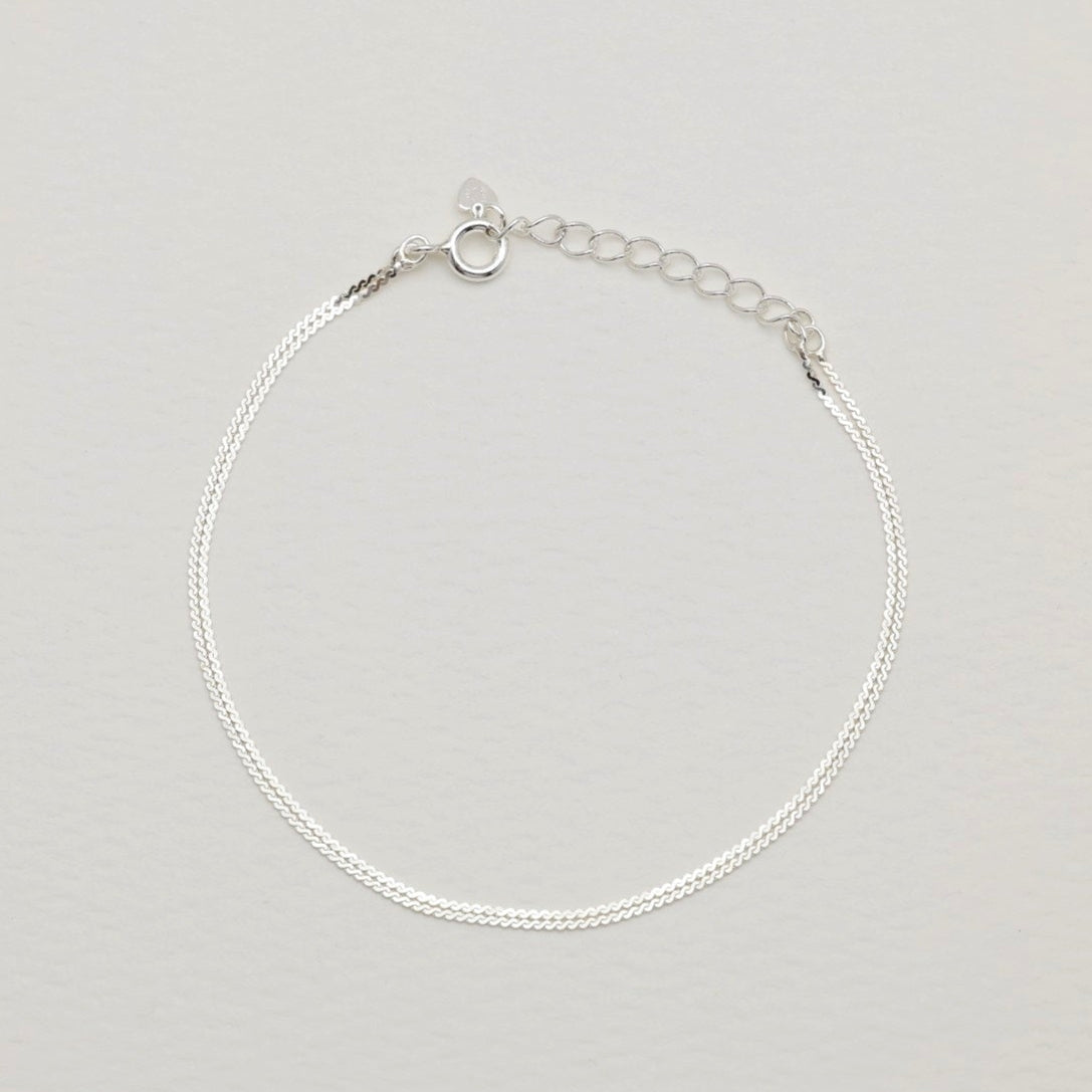 Sterling silver dual-strand bracelet with polished finish and extension chain on cream background