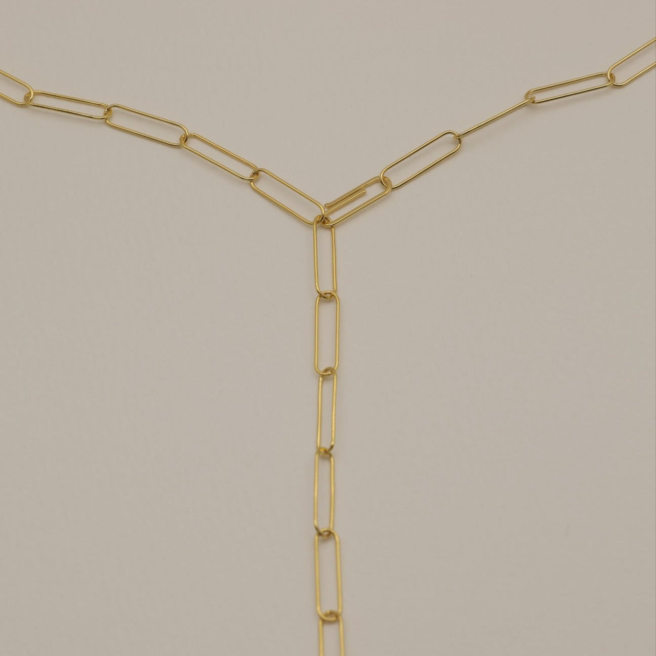 A detailed photograph of a long gold chain necklace with elongated links arranged in a Y-shape against a neutral background.