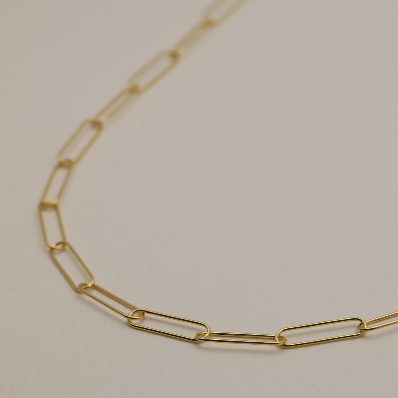 A close-up shot highlighting the fine elongated links of the gold vermeil chain necklace on a cream surface.