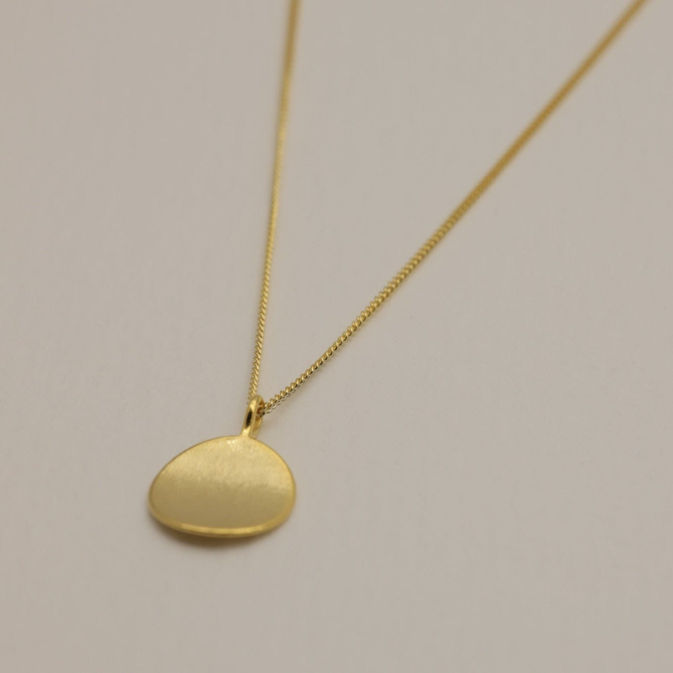A close-up of the round gold vermeil pendant with a brushed finish, ideal for engraving.