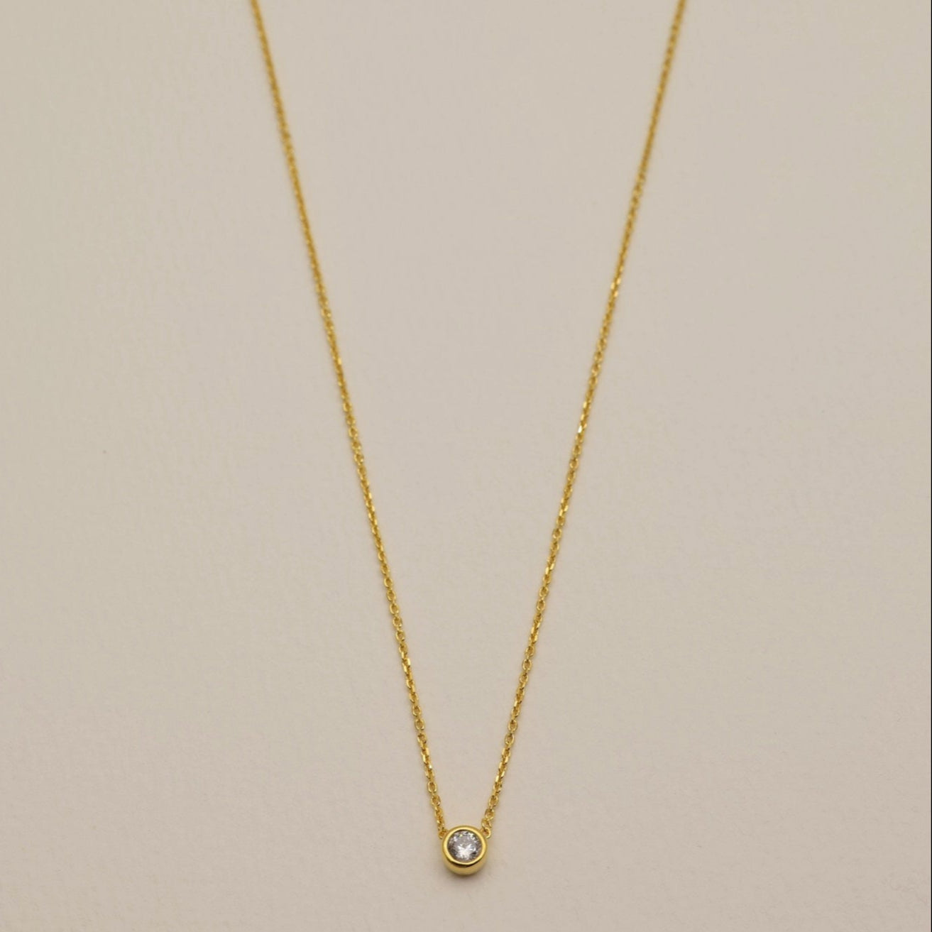 Delicate gold vermeil necklace with round cubic zirconia bezel pendant on cream background