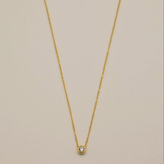 Delicate gold vermeil necklace with round cubic zirconia bezel pendant on cream background