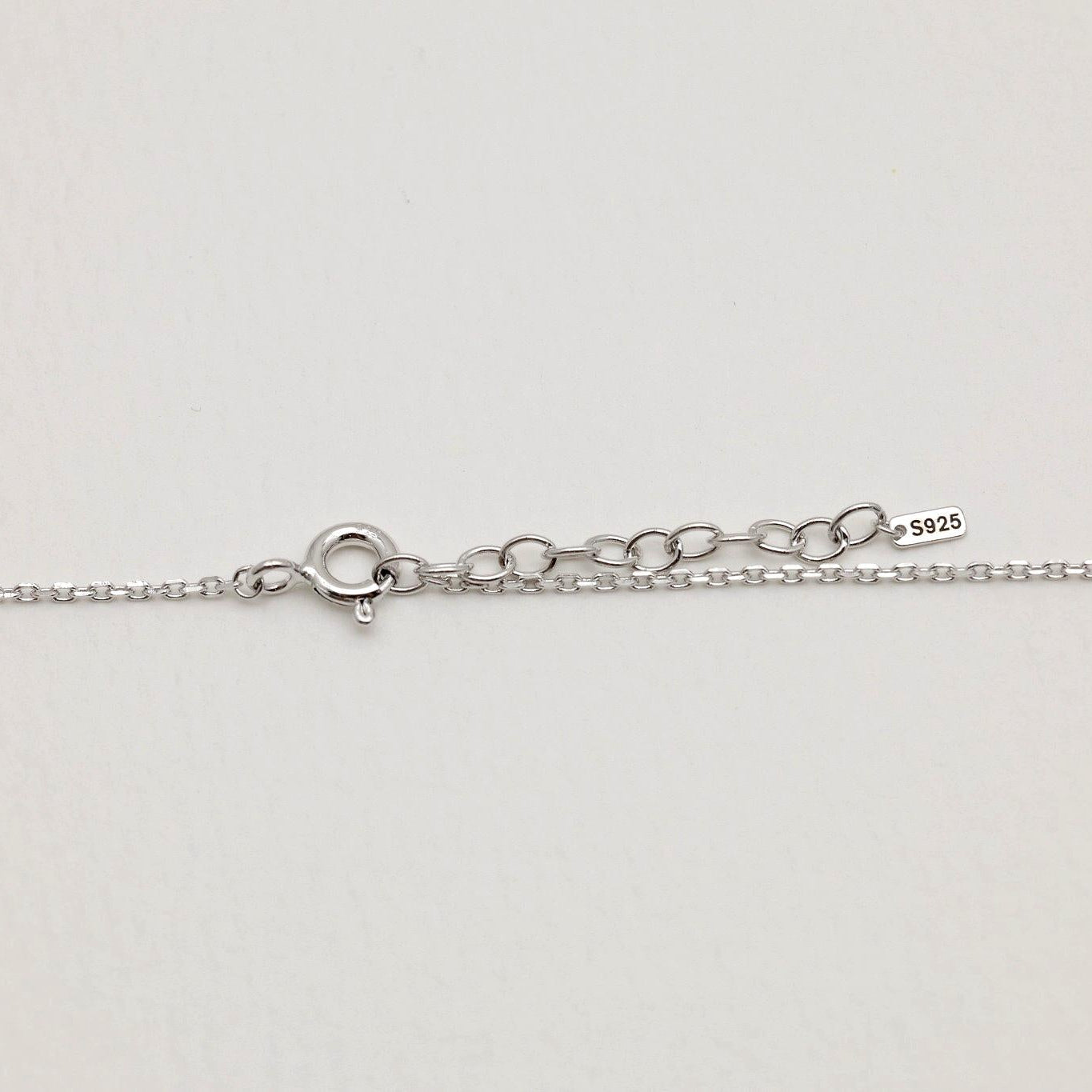 Close-up of the clasp and extender of a 925 sterling silver necklace, marked with an "S925" tag, photographed on a soft neutral background.

