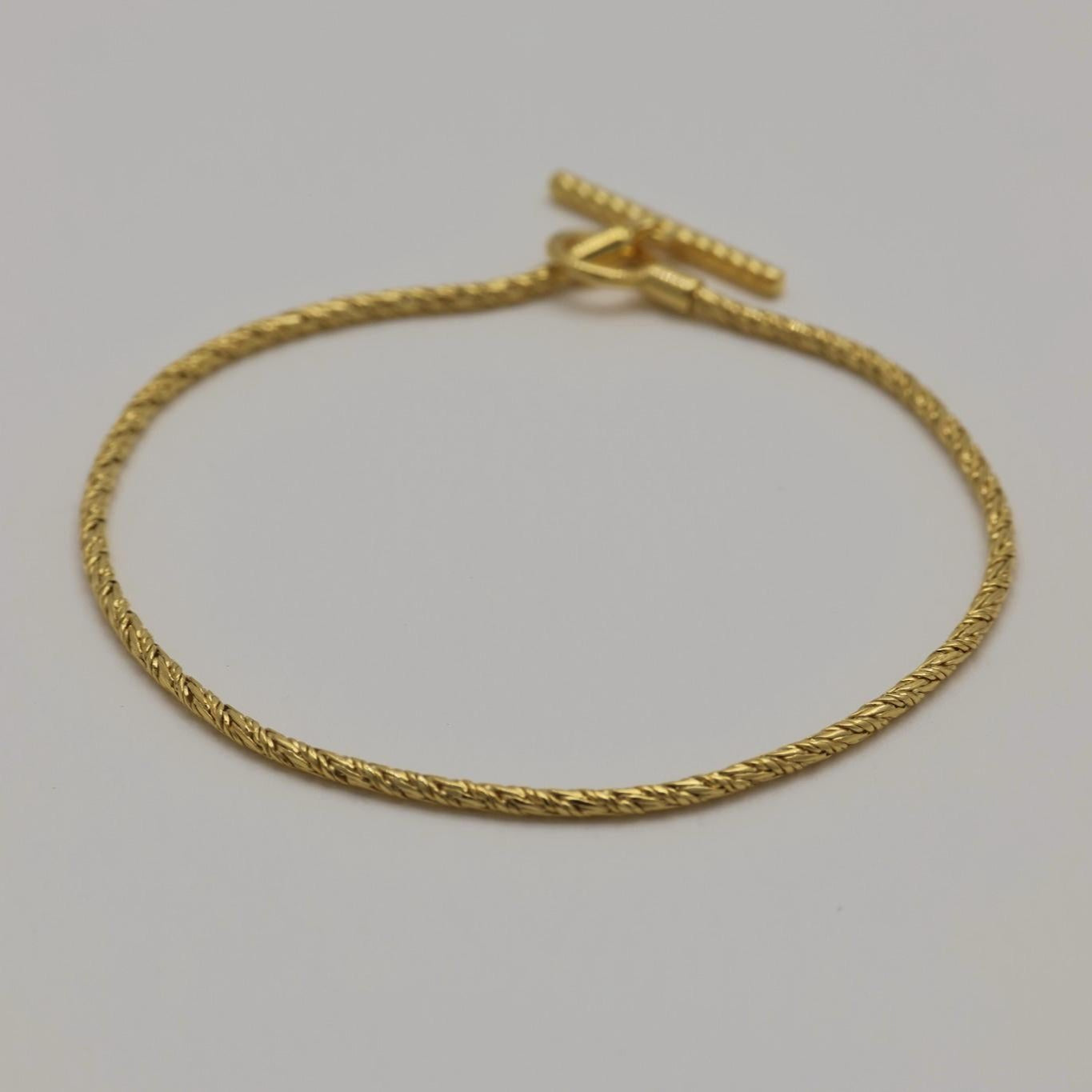 Close-up of twisted rope chain bracelet in gold vermeil with toggle clasp, styled in a circular shape.