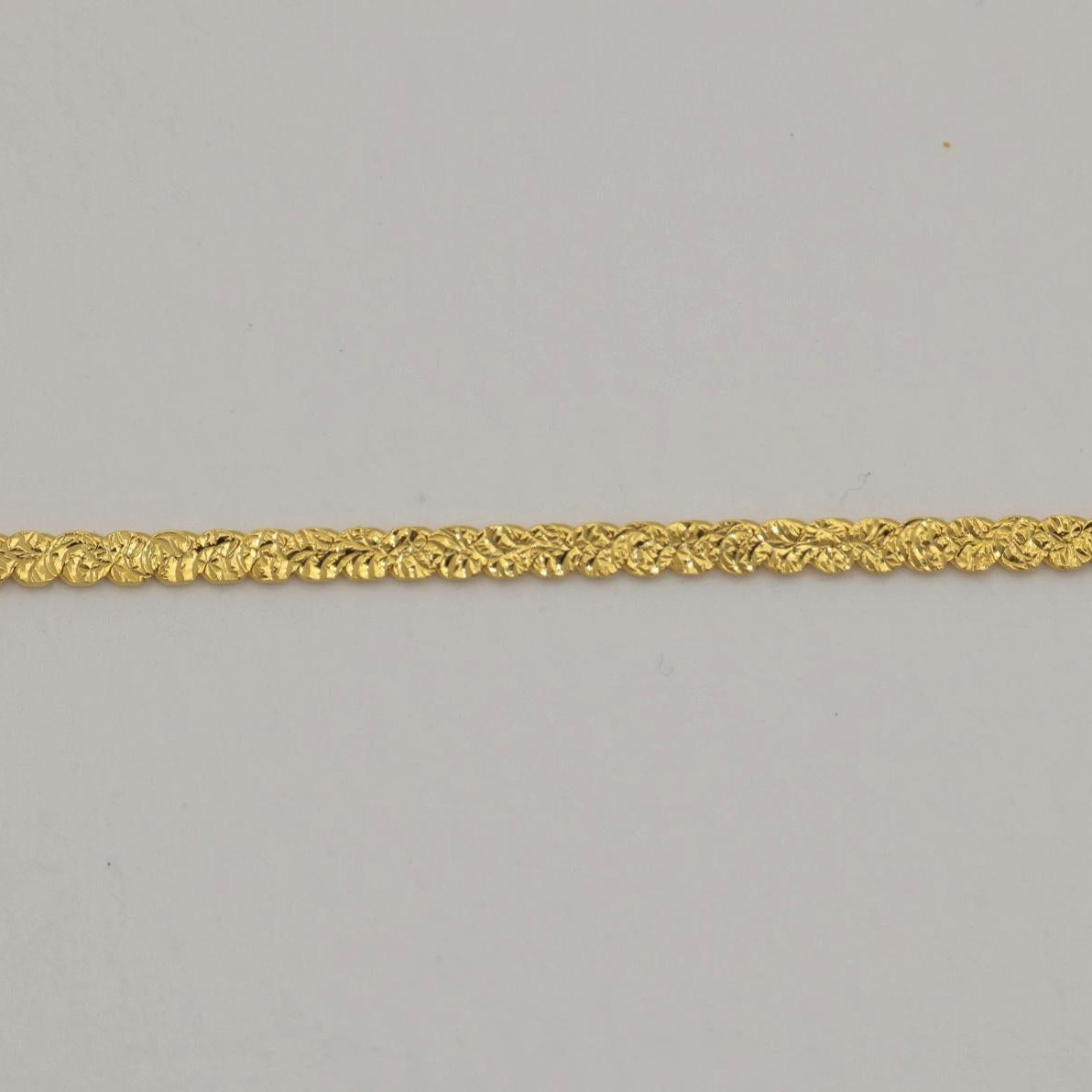 Close-up of a gold vermeil flat herringbone bracelet with polished surface and lobster clasp on neutral background.