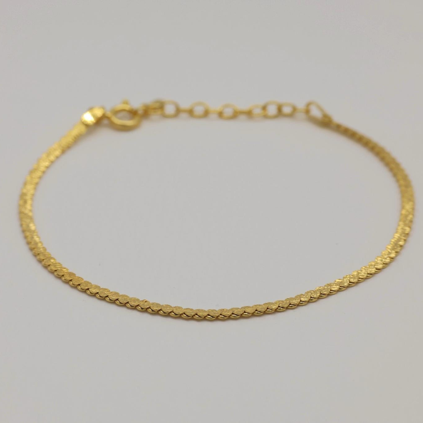 Angled perspective of a gold vermeil herringbone bracelet laid flat with visible clasp and extension chain.