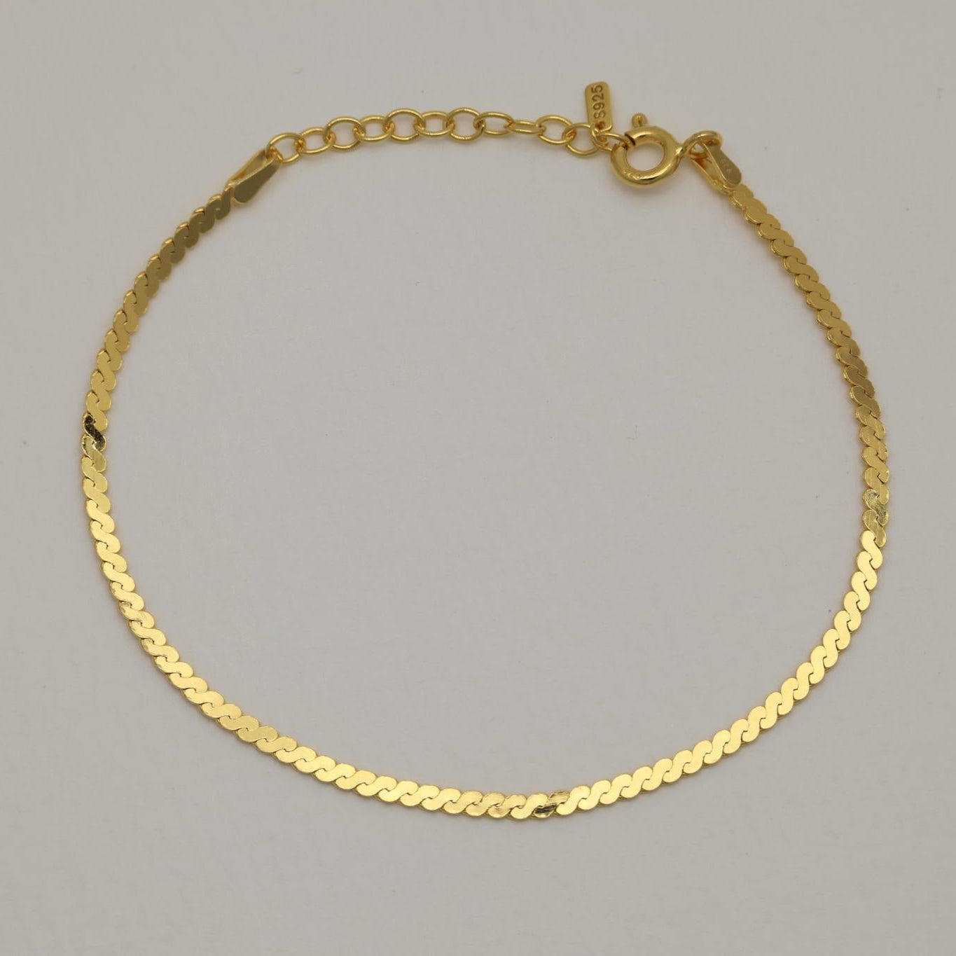 Overhead shot of a minimalist gold vermeil bracelet with flat links, softly curved into a closed loop on a plain backdrop