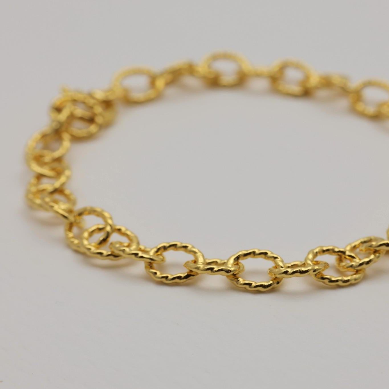 Close-up view of a gold vermeil bracelet showing round ripple-textured links in sharp focus against a neutral background.


