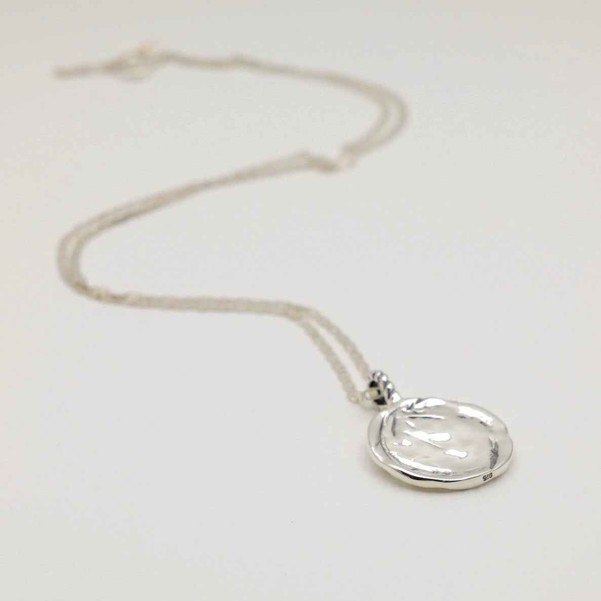 Silver necklace with a clear pendant on a light gray background