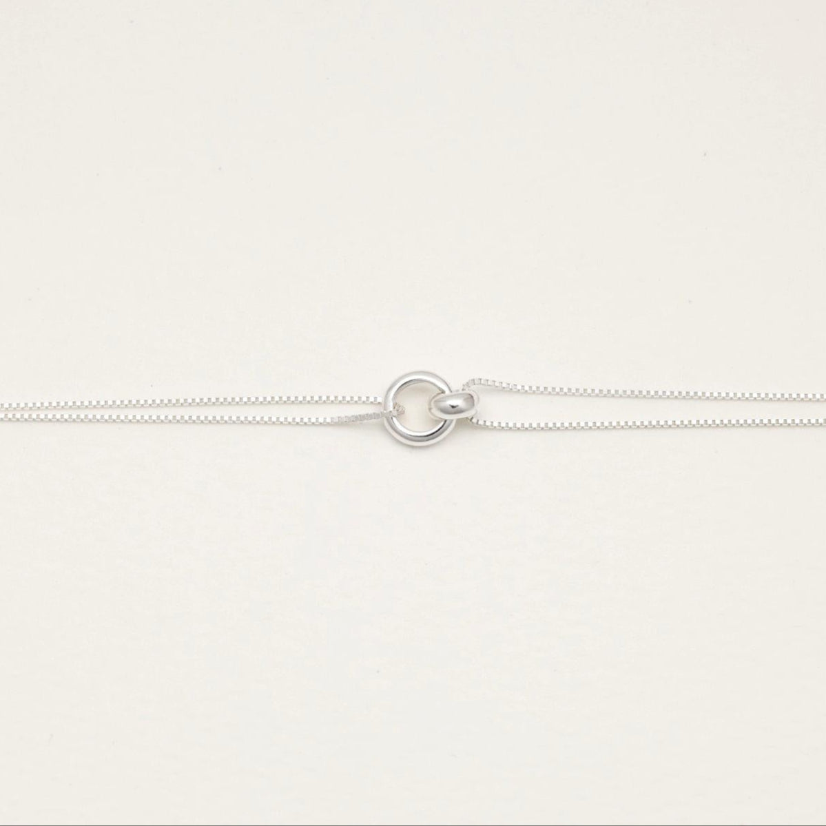 Sterling silver dual-chain bracelet with sculptural ring detail, laid flat on a cream background.