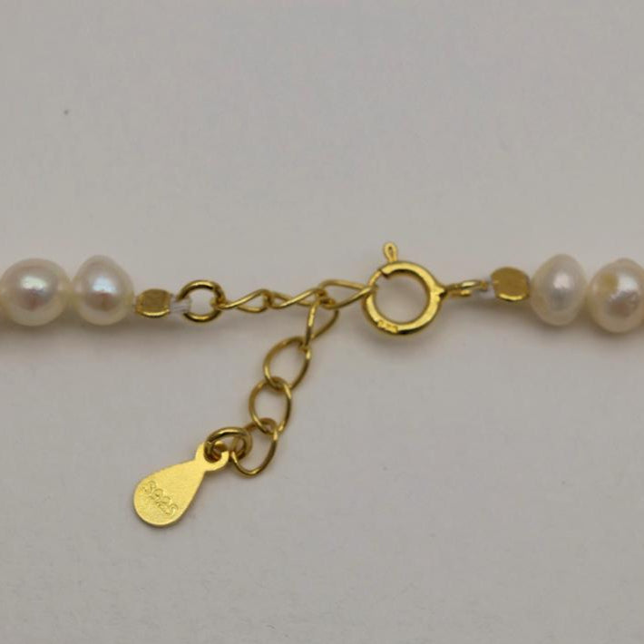 Pearl necklace with a gold clasp and tag on a light gray background