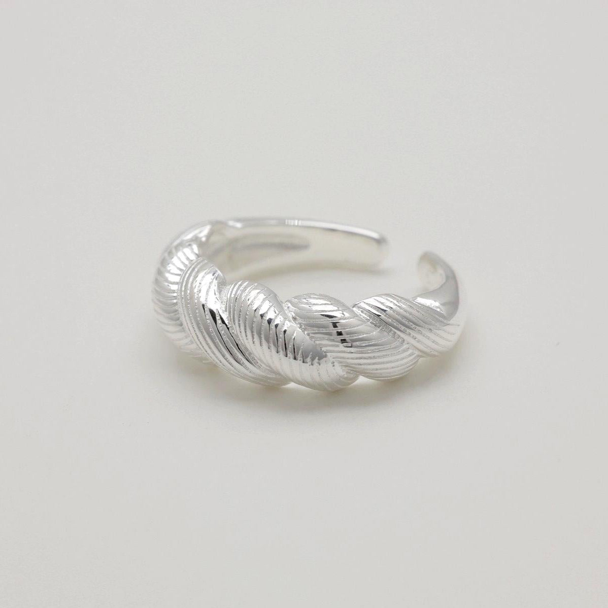 Close-up of sterling silver braided ring with ridged texture on a light background