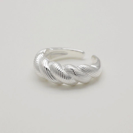 Close-up of sterling silver braided ring with ridged texture on a light background