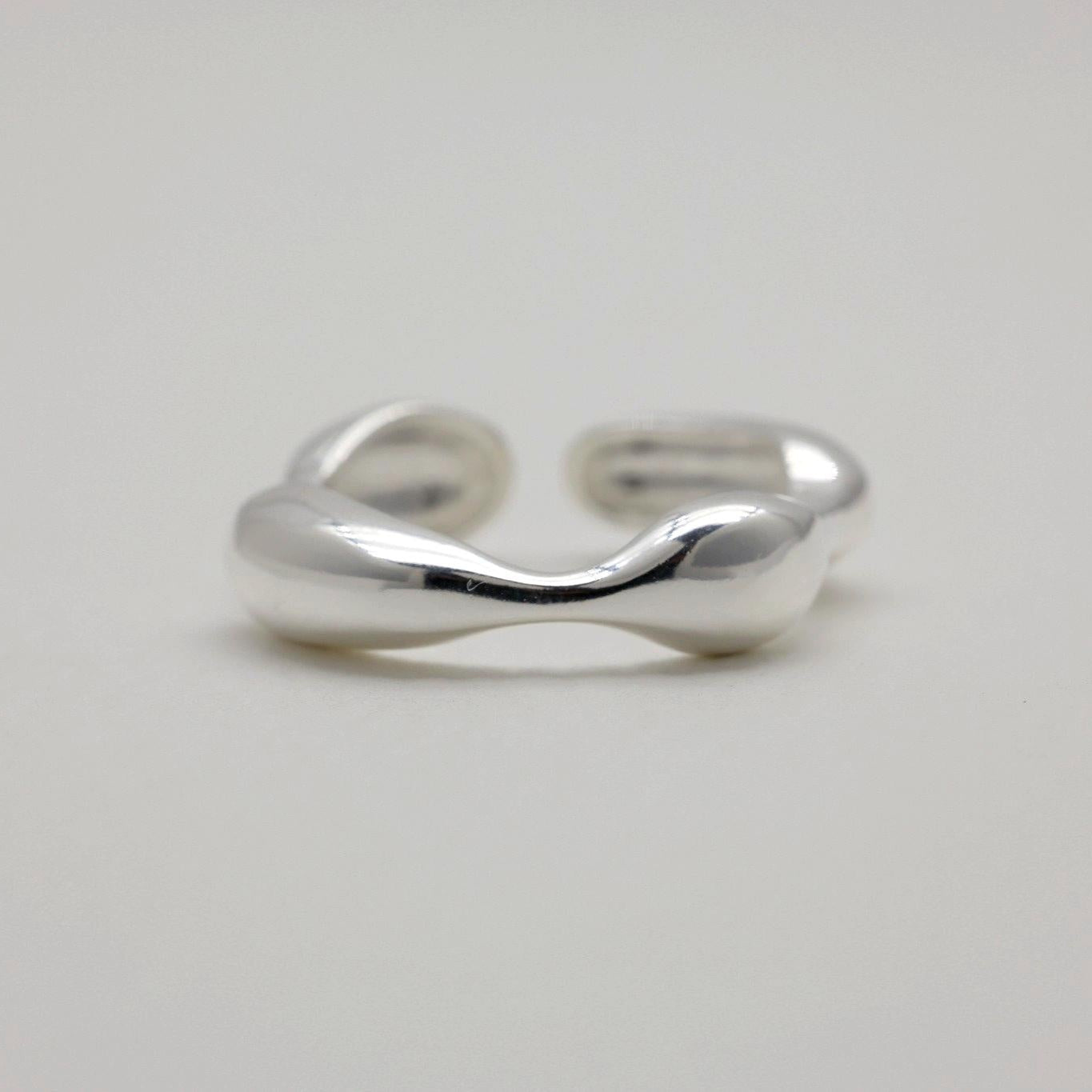 Adjustable sculptural silver ring with fluid curves and polished finish, open-ended band design.