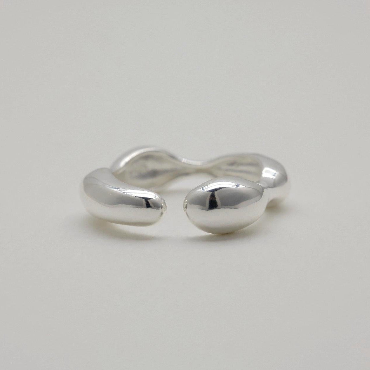Adjustable sculptural silver ring with fluid curves and polished finish, open-ended band design.
