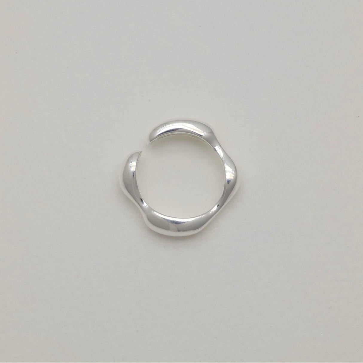 Adjustable sculptural silver ring with fluid curves and polished finish, open-ended band design.