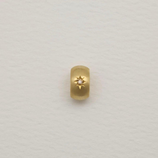 Gold oval pendant with a matte finish and engraved starburst set with a tiny diamond, photographed on a soft white background.