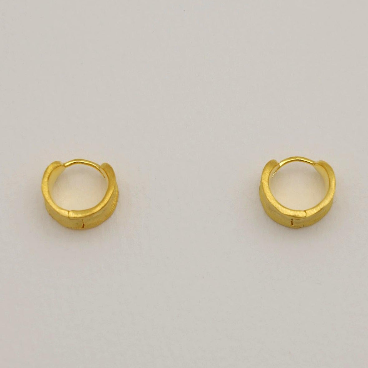 A pair of sculptural matte gold vermeil mini hoops with softly curved surfaces and a subtle, satin finish.