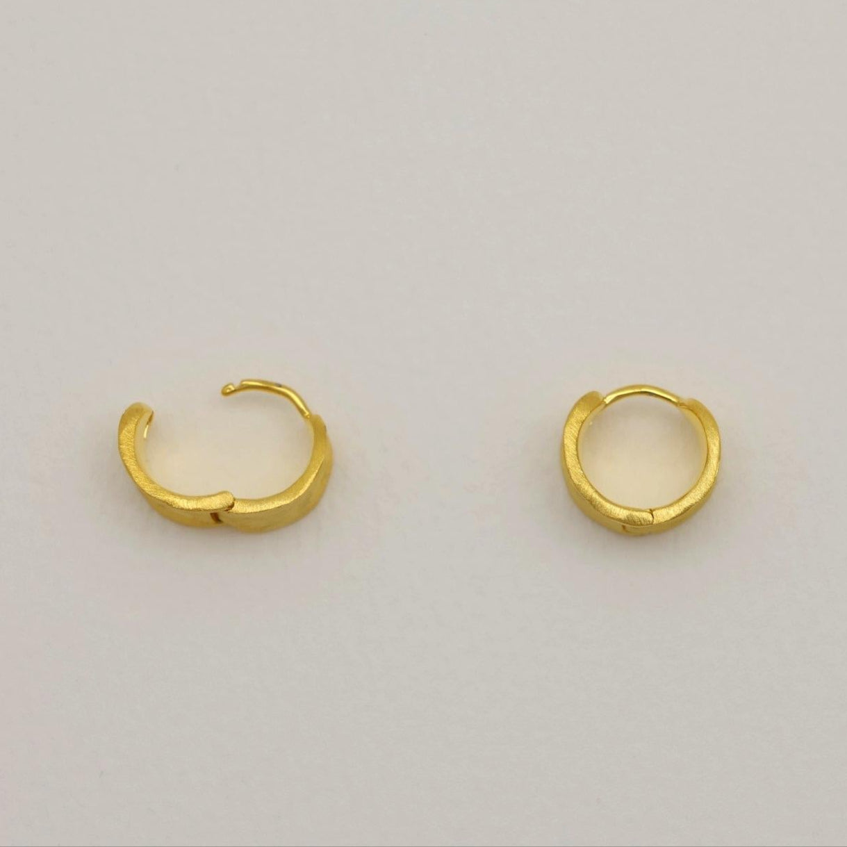 A pair of sculptural matte gold vermeil mini hoops with softly curved surfaces and a subtle, satin finish.