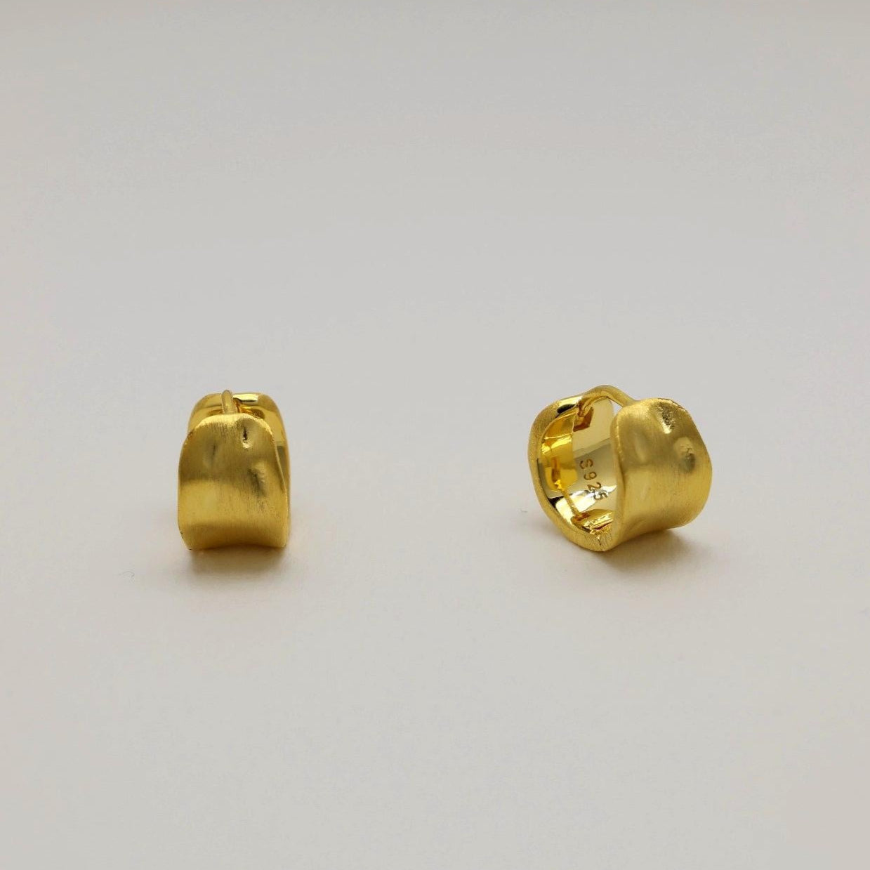 A pair of sculptural matte gold vermeil mini hoops with softly curved surfaces and a subtle, satin finish.