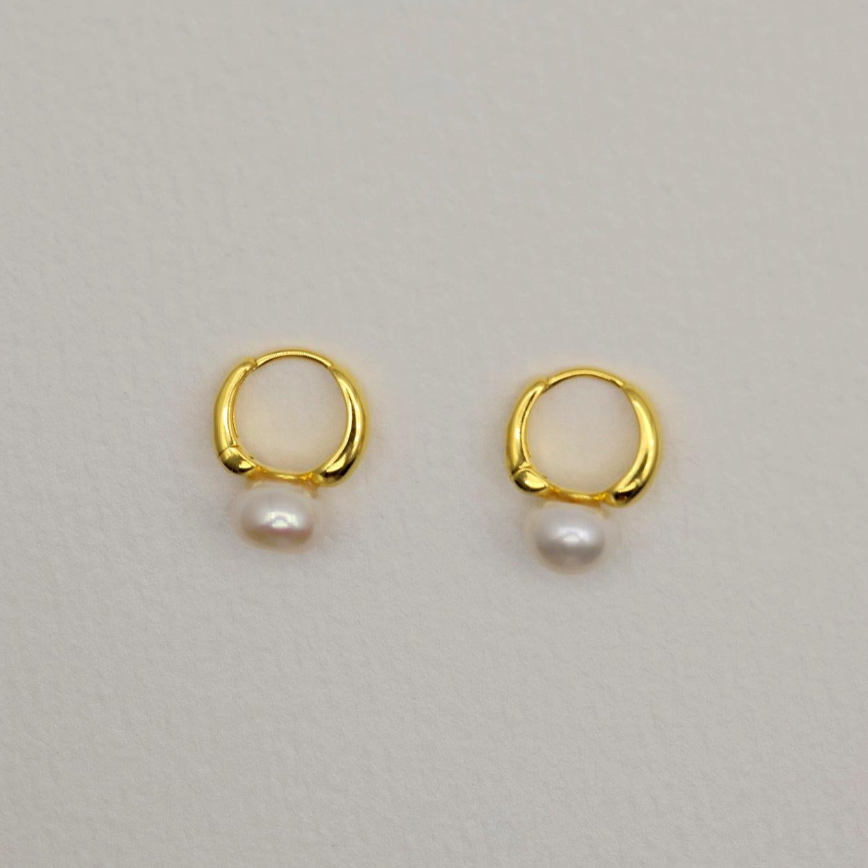 Gold vermeil huggie earrings with natural white pearl drops, photographed on a soft neutral background.