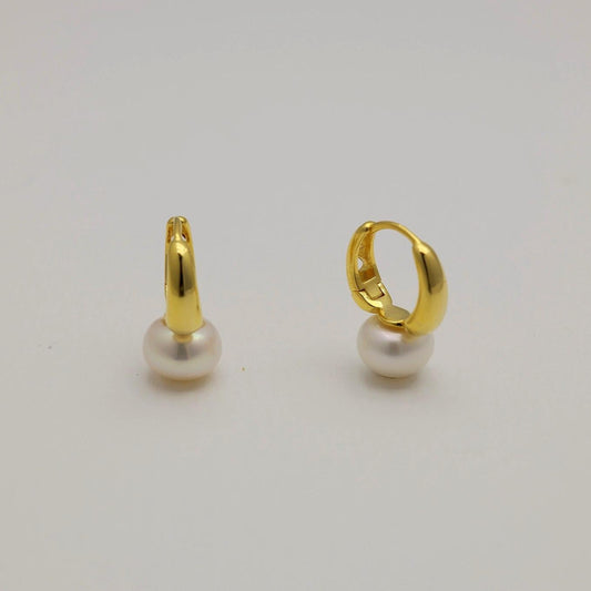 Gold vermeil huggie earrings with natural white pearl drops, photographed on a soft neutral background.