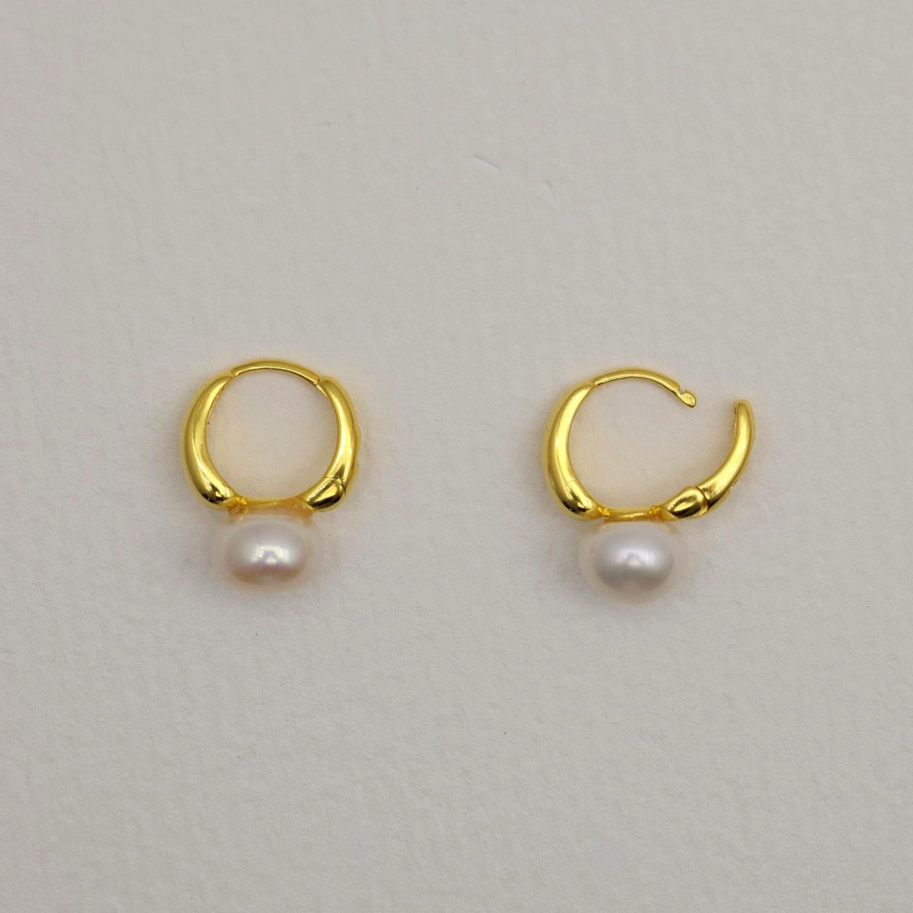 Gold vermeil huggie earrings with natural white pearl drops, photographed on a soft neutral background.