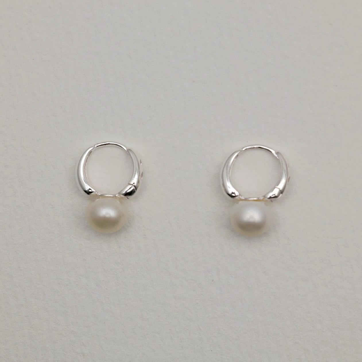 Sterling silver huggie earrings with natural freshwater pearls, minimalist curved design.