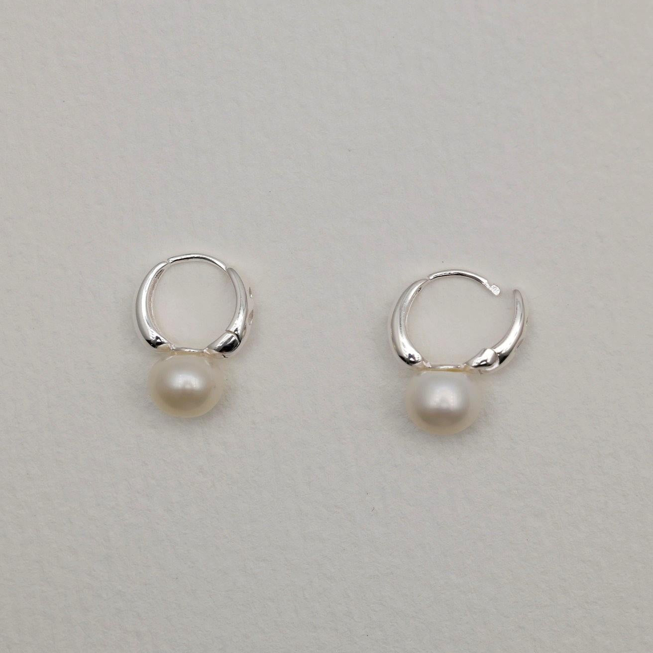 Sterling silver huggie earrings with natural freshwater pearls, minimalist curved design.