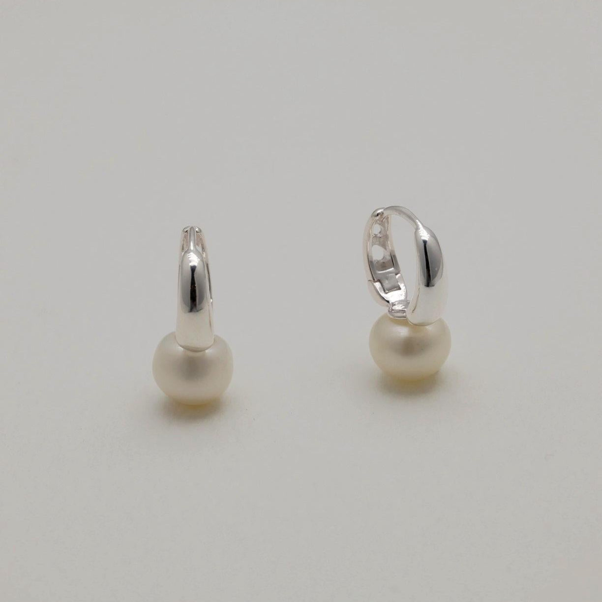Sterling silver huggie earrings with natural freshwater pearls, minimalist curved design.