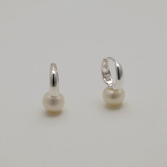 Sterling silver huggie earrings with natural freshwater pearls, minimalist curved design.